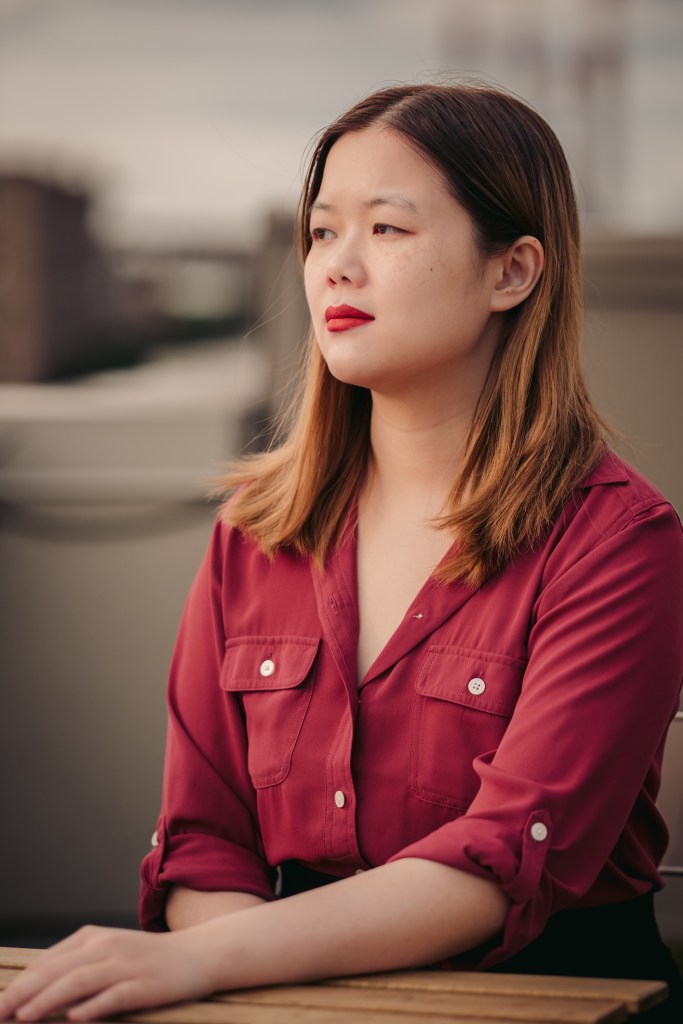 Headshot of Kailee Pedersen, a Chinese American writer with dark brown hair and brown eyes wearing a pink shirt